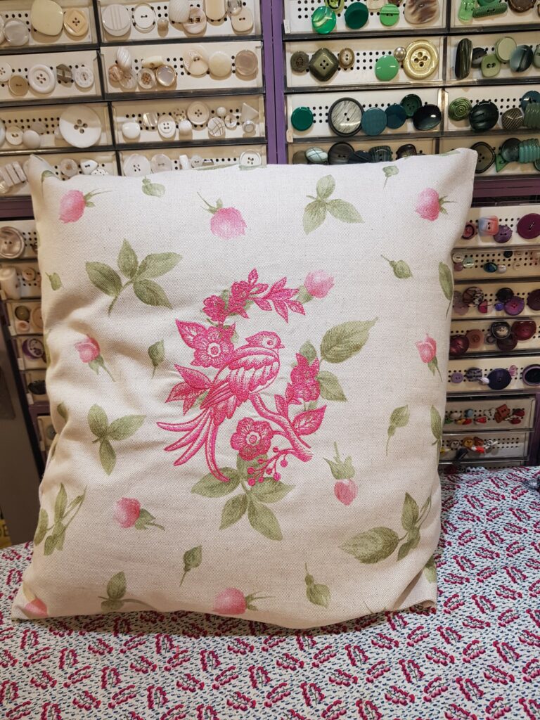 Un coussin avec, brodé dessus, un oiseau posé sur une branche