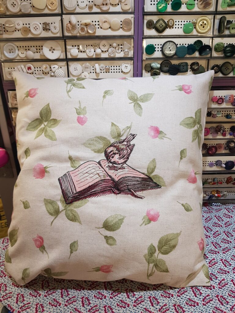 Un coussin avec, brodé dessus, un oiseau posé sur un livre